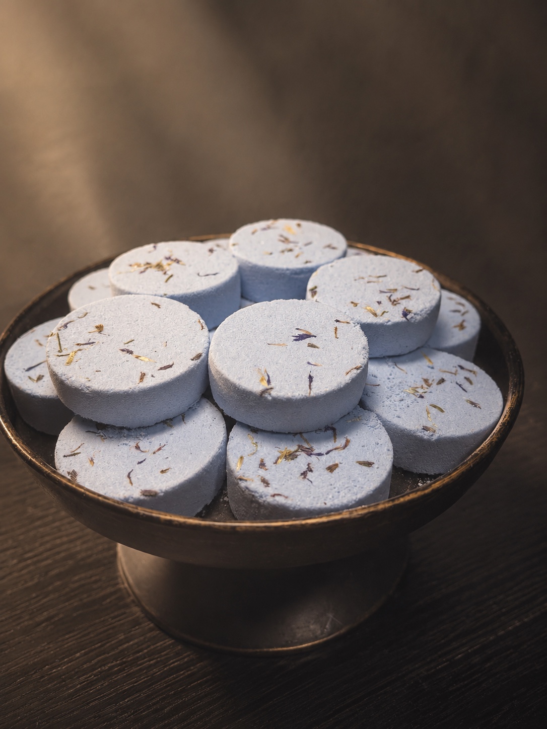 Handcrafted blue Moonlit Dream rounds topped with botanicals on a dark display tray